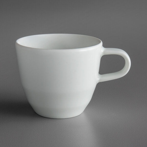 A Schonwald bone white porcelain espresso cup with a white handle on a gray surface.