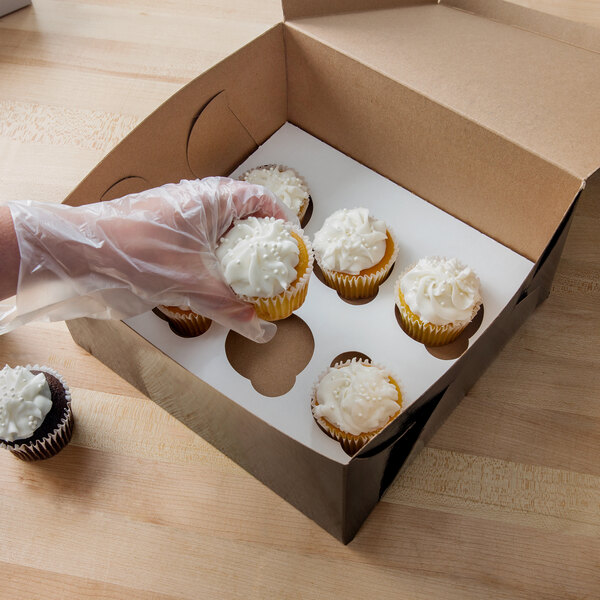 A hand putting a white frosted cupcake in a Baker's Mark black cupcake box.