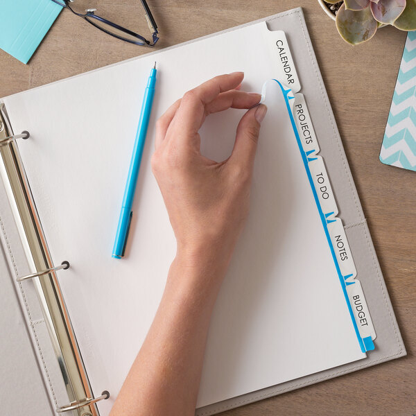 A hand writing on Avery white paper divider tabs with a pen.