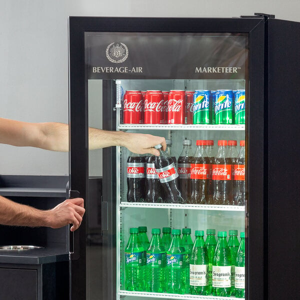 A man opening the glass door of a Beverage-Air refrigerated cooler filled with soda bottles.