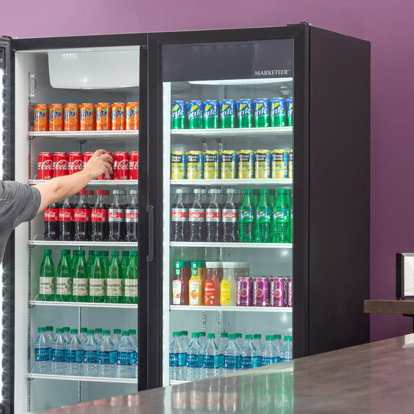 A man standing near a Beverage-Air Marketeer refrigerator filled with drinks.