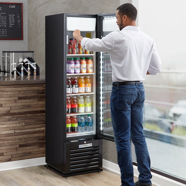 A man standing in front of a Beverage-Air Marketeer glass door refrigerator full of drinks.