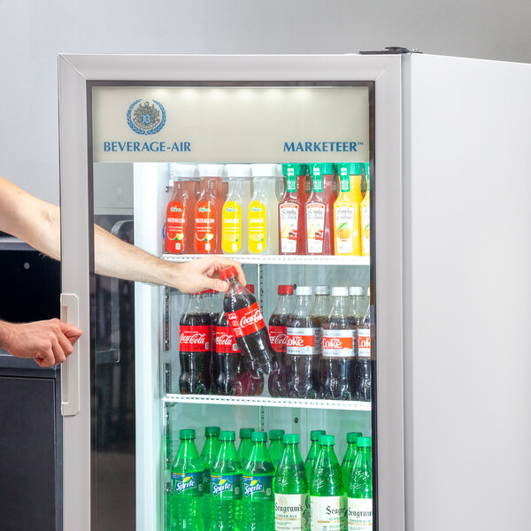 A person opening a Beverage-Air white glass door refrigerator to get a drink.