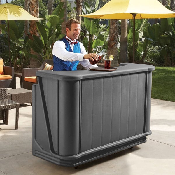 A man standing behind a Cambro portable bar with a drink.