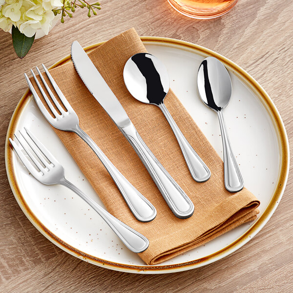 A plate with Acopa Edgeworth stainless steel flatware on it, including a fork and knife.
