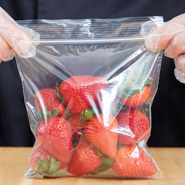 A gloved hand holding a 6" x 6" plastic bag of strawberries.