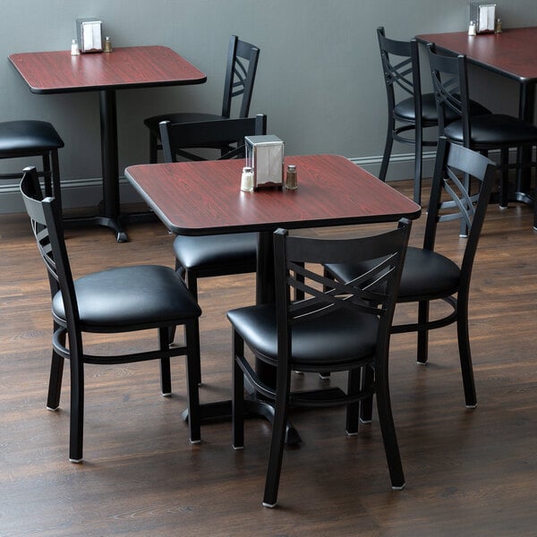 A Lancaster Table & Seating dining set with a black table and chairs, salt and pepper shakers on the table.