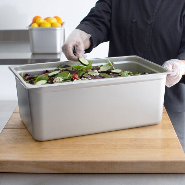A person putting vegetables in a Choice stainless steel steam table pan on a counter.
