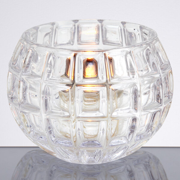 A Sterno Atlas glass votive candle holder with a lit candle inside.