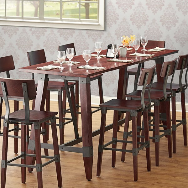 A Lancaster Table & Seating solid wood live edge table top with a mahogany finish on a table with wine glasses and chairs.