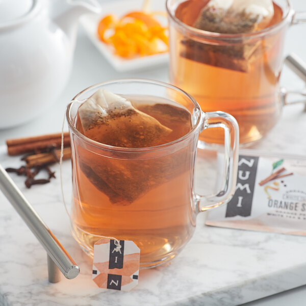 A glass mug of Numi Organic Orange Spice tea with a tea bag in it.