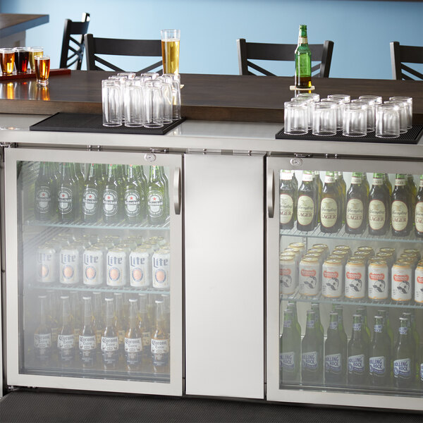 A glass door back bar refrigerator full of beer bottles and glasses.