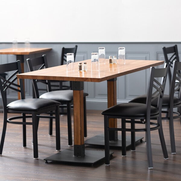 A Lancaster Table & Seating dining table with a wooden surface and black metal legs, surrounded by black chairs.