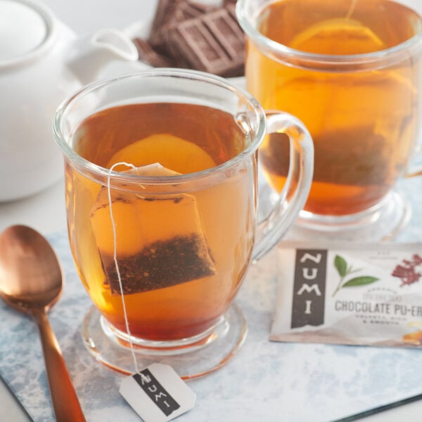 A glass mug of Numi Organic Chocolate Pu-Erh Tea with a tea bag in it on a tray.
