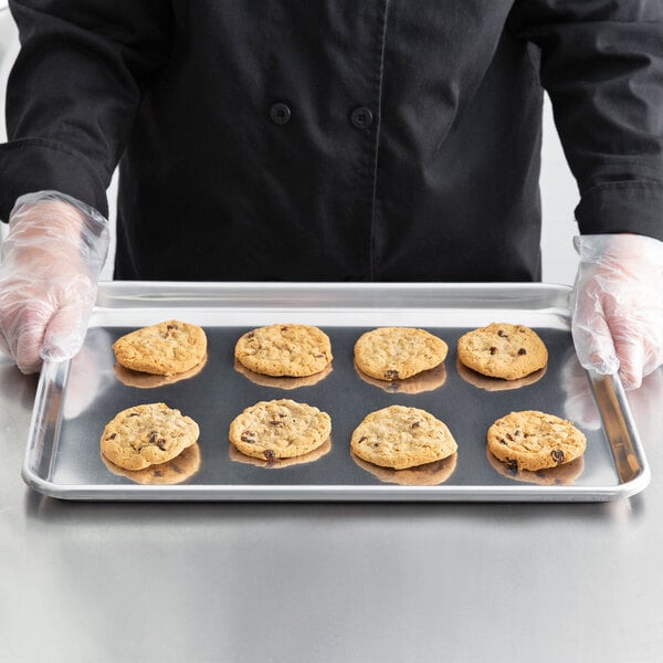 A person in a chef's uniform holding a Baker's Mark tray of cookies.