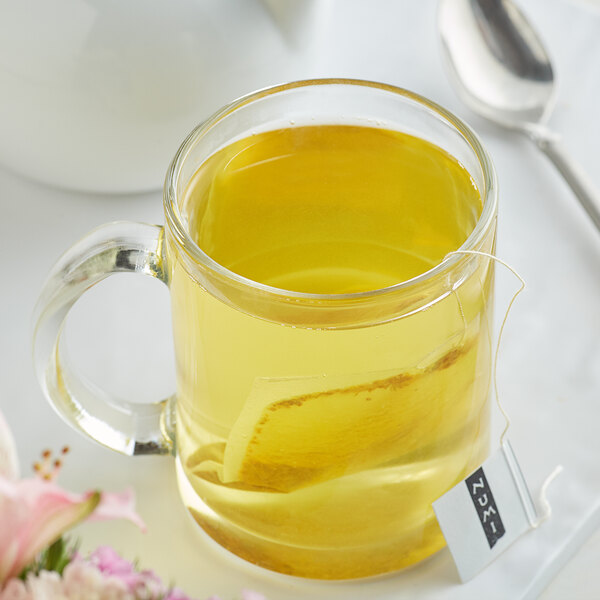A glass mug of yellow Numi Organic Three Roots Turmeric Tea with a tea bag in it.