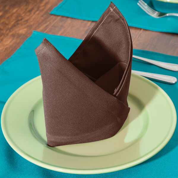 A folded brown Intedge cloth napkin on a plate.