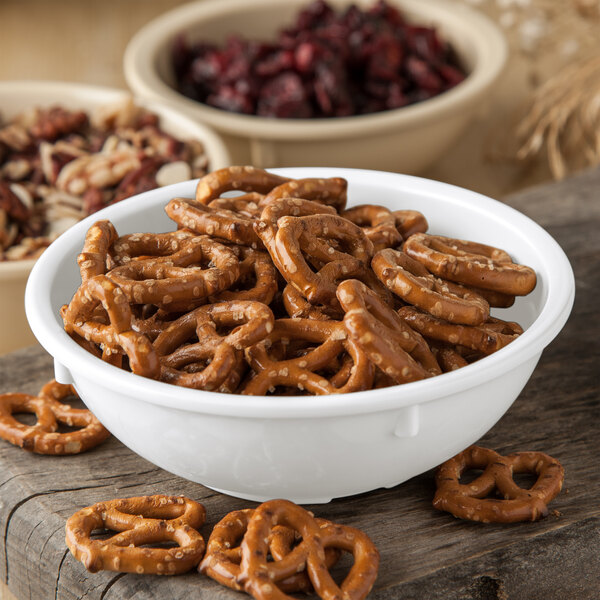 A Carlisle white melamine nappie bowl filled with pretzels and nuts on a table.