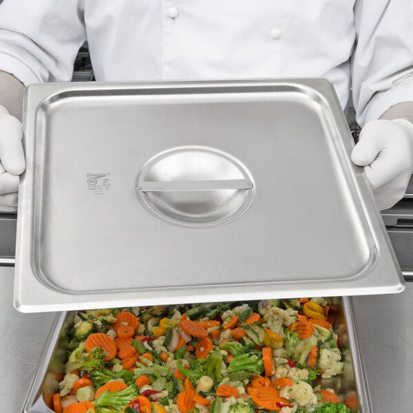 A chef using a Vollrath Super Pan V stainless steel lid to cover a tray of food.