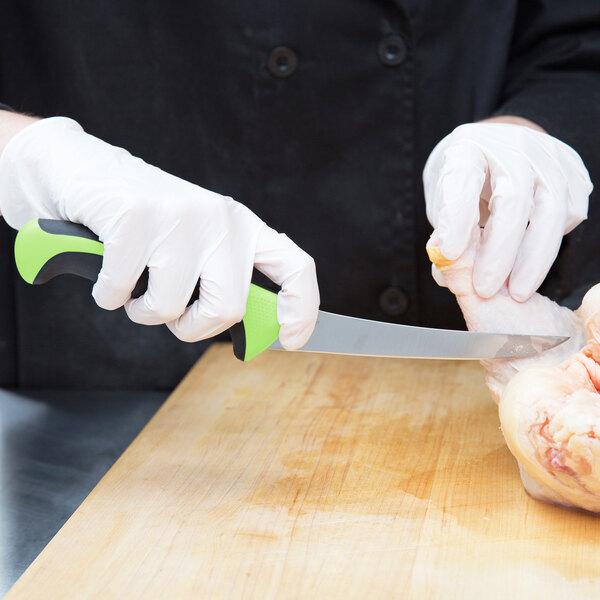 A person in white gloves using a green and black Mercer Culinary Millennia curved stiff boning knife to cut chicken.