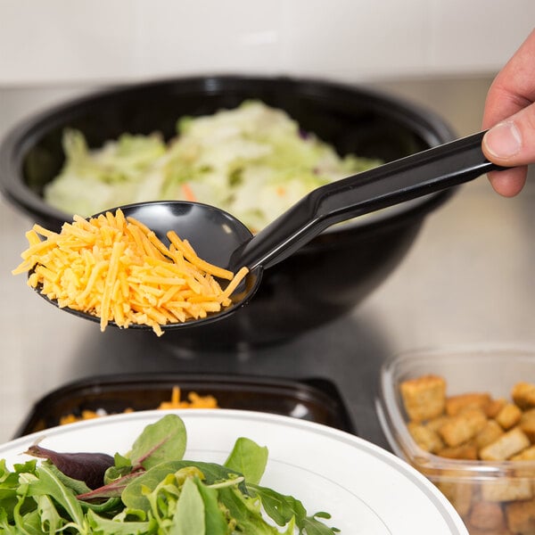 A person using a Thunder Group solid salad bar spoon to serve shredded cheese.
