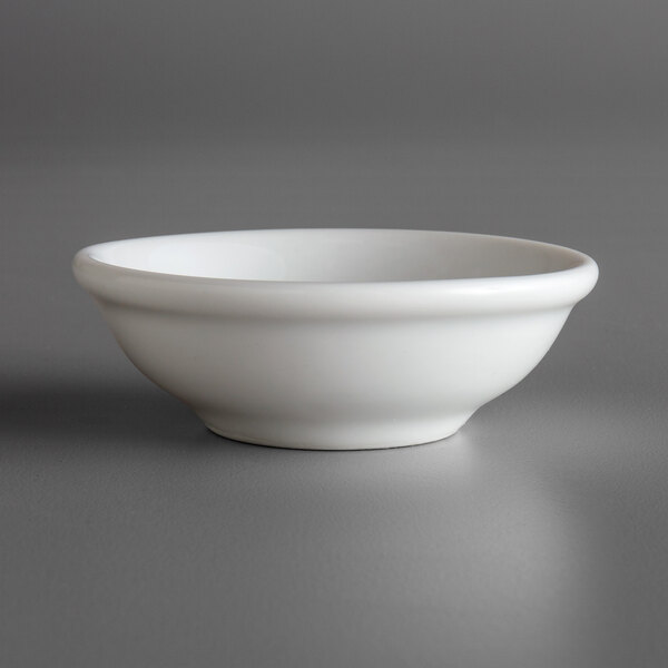 A Oneida Fusion bright white porcelain sauce dish on a gray surface.