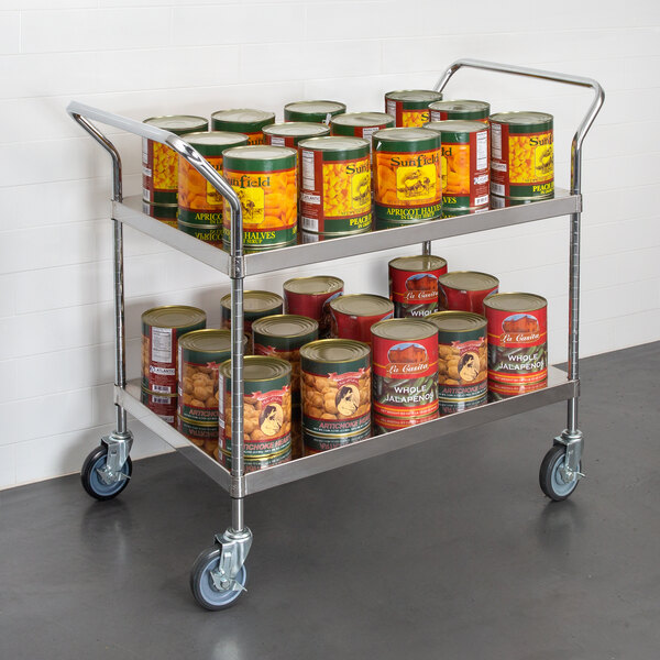 A Regency stainless steel utility cart full of canned food.
