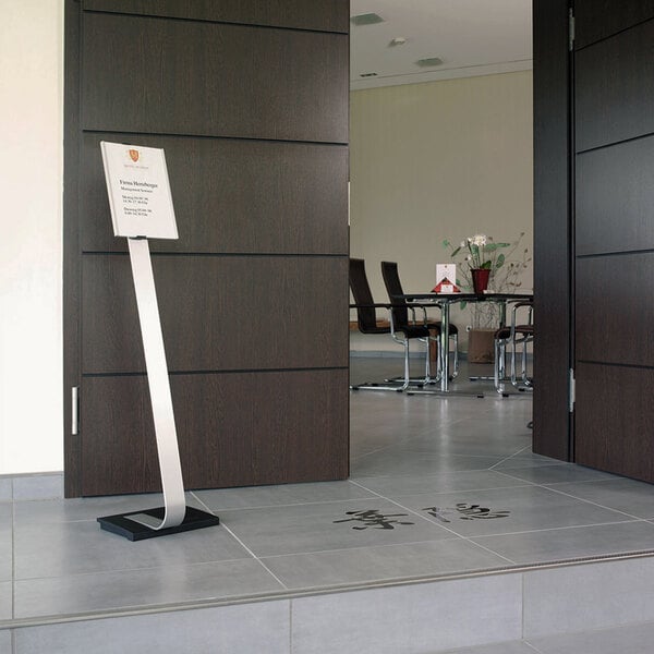 A Durable metal stand with adjustable insert space holding a sign on the floor in front of a door.