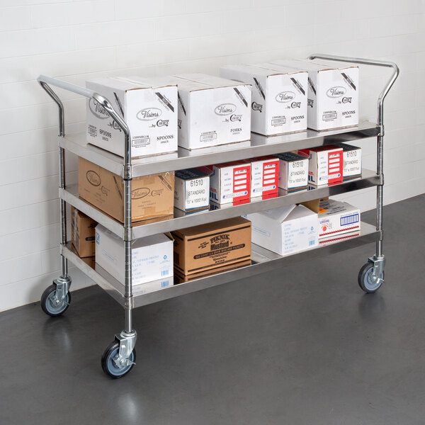 A Regency stainless steel utility cart with boxes on metal shelves.