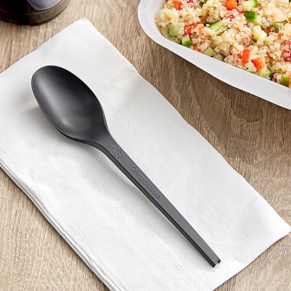 A white container with food and a black EcoChoice Heavy Weight CPLA plastic spoon on a table.