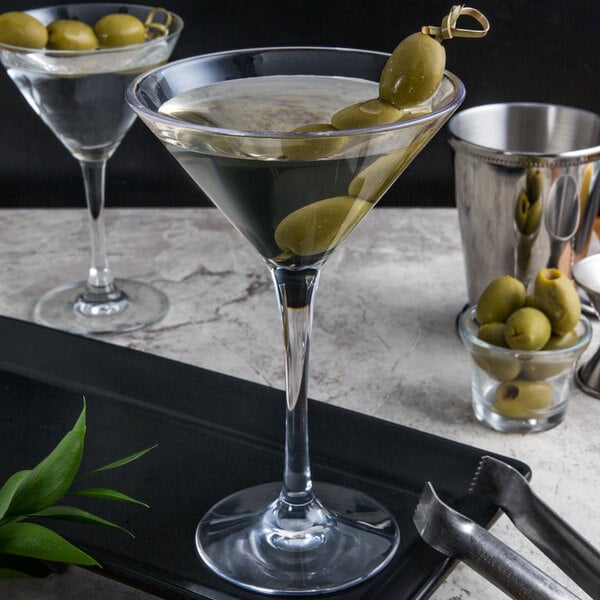 Two Libbey plastic martini glasses with olives on a counter.