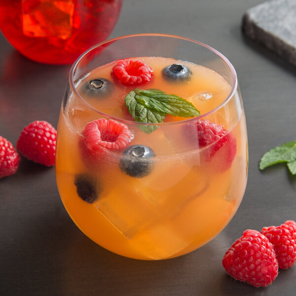 A Libbey plastic stemless wine glass filled with orange liquid and garnished with berries and mint.