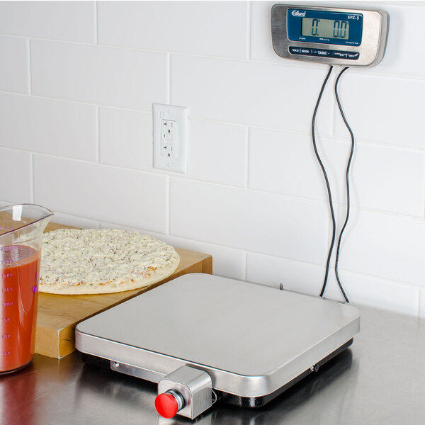An Edlund stainless steel digital pizza scale on a counter with a pizza.