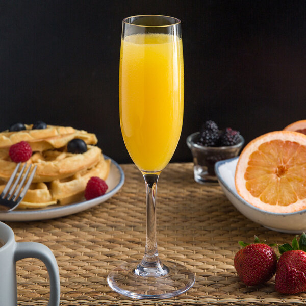 A Libbey Tritan plastic champagne flute filled with orange juice on a breakfast table with waffles and fruit.