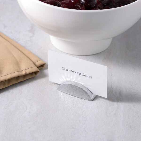 An American Metalcraft hammered aluminum half moon table card holder with a name card in a bowl of cranberry sauce on a table.