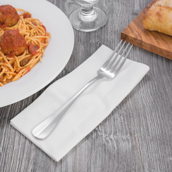 Oneida Baguette 18/10 stainless steel table fork on a napkin next to a plate of spaghetti.