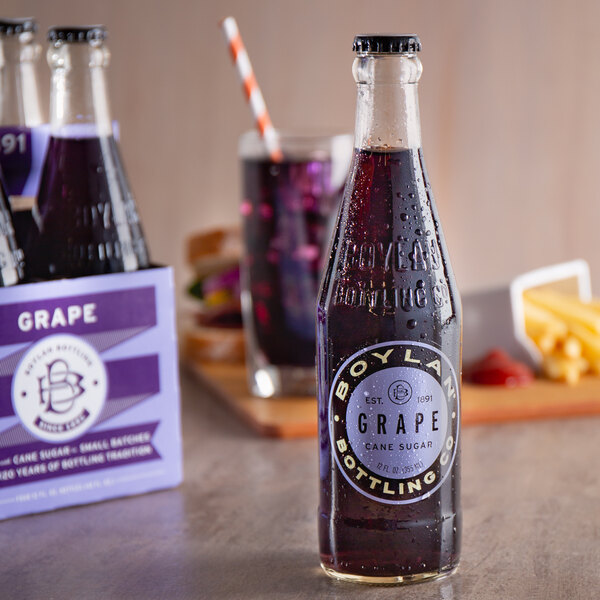 A bottle of Boylan grape soda on a table next to a box of chips.