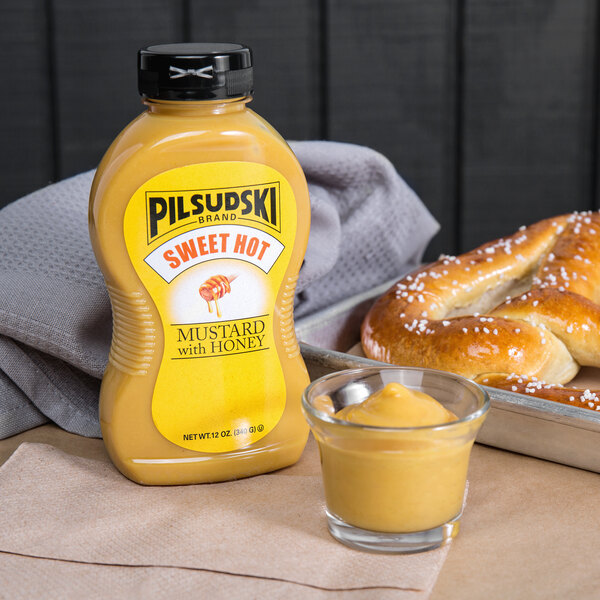 A Pilsudski Sweet Hot Honey Mustard upside down squeeze bottle on a table next to pretzels.