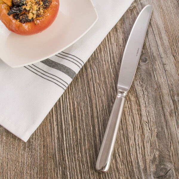 An Oneida Baguette stainless steel dessert knife on a white napkin next to a plate of food.