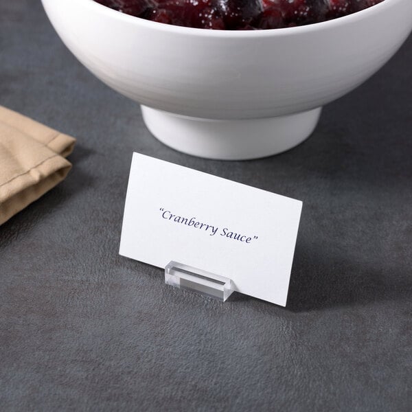 A white table with American Metalcraft clear acrylic table card holders holding a place card over a bowl of cranberry sauce.