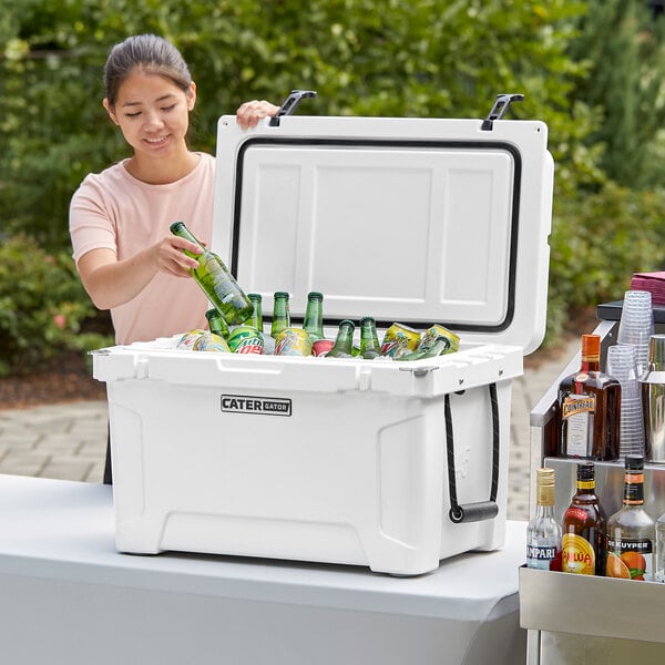 A woman putting green bottles into a white CaterGator outdoor cooler.