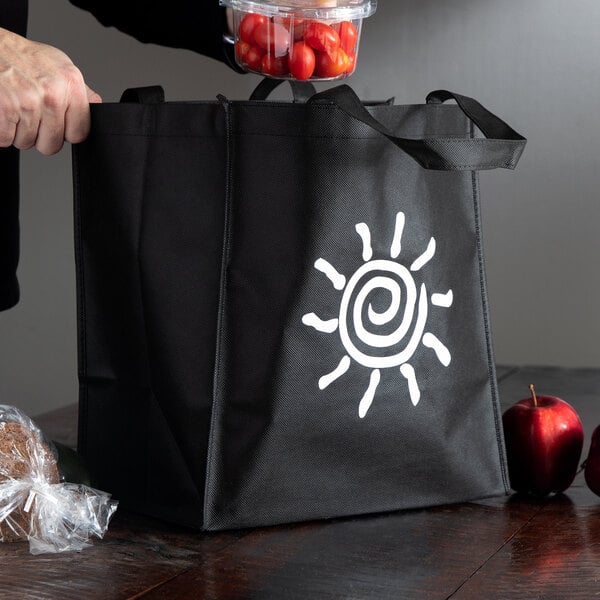 A person holding a black LK Packaging reusable shopping bag with a white sun on it.