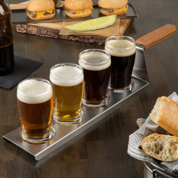 A Tablecraft stainless steel flight paddle with burgers and beer glasses on a table.