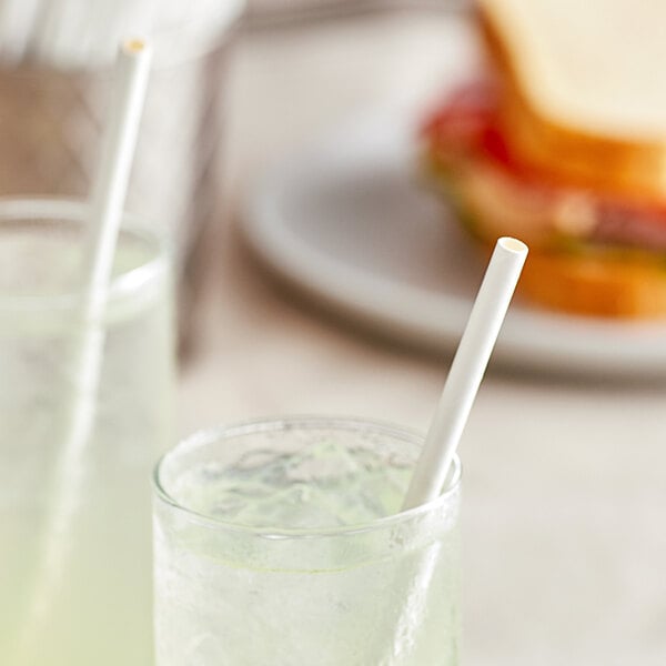 A glass of green drink with a EcoChoice white paper straw in it on a table with sandwiches.
