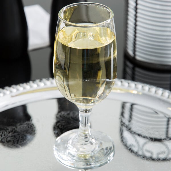 A close-up of a Libbey white wine glass filled with white wine on a silver tray.