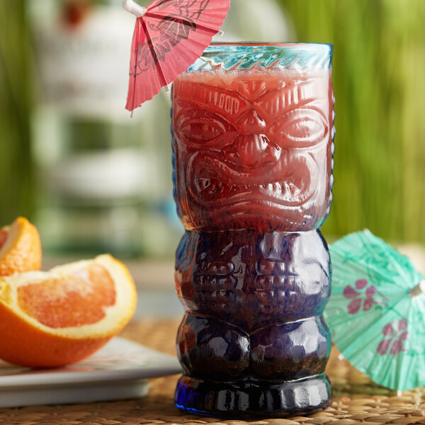 A Blue Lagoon Tiki drink in an OG Blue Lagoon Tiki Glass with an umbrella and orange slices.