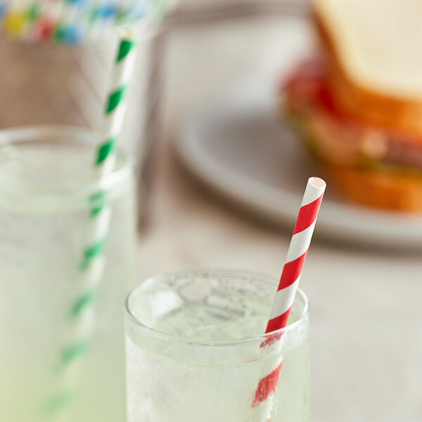 A glass with ice and a red and white striped EcoChoice paper straw in it.