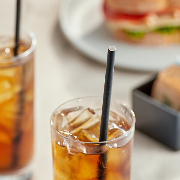 A glass of iced tea with an EcoChoice black paper straw in it on a table with a sandwich.
