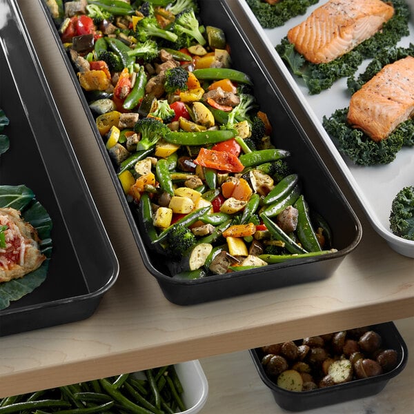 A black Cambro market pan filled with vegetables and salmon on a table.