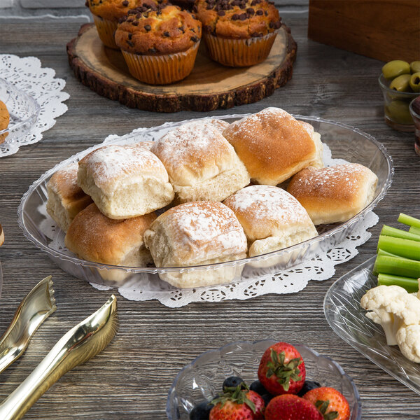 A table with a variety of food items including rolls and muffins served on Fineline Crystal Plastic catering trays.